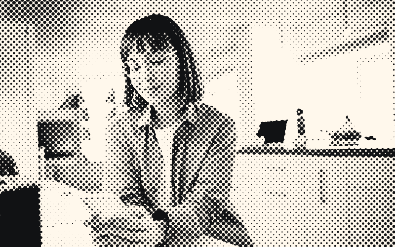 Une femme à lunettes, appuyée au comptoir de sa cuisine, consulte son téléphone.