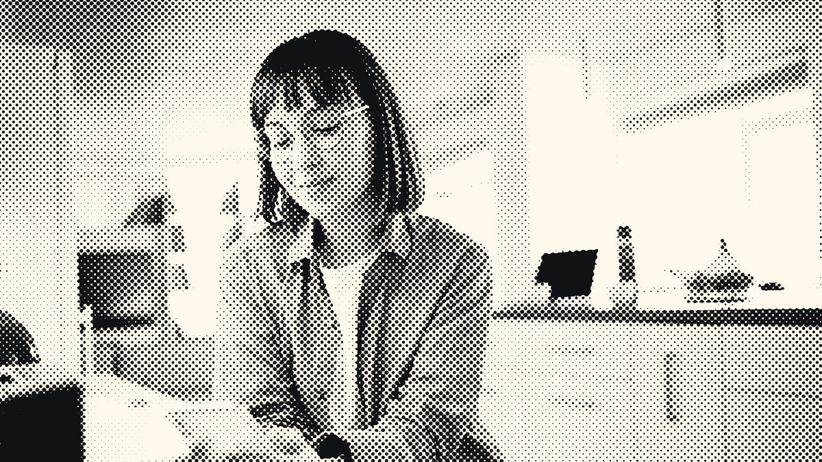 Une femme à lunettes, appuyée au comptoir de sa cuisine, consulte son téléphone.